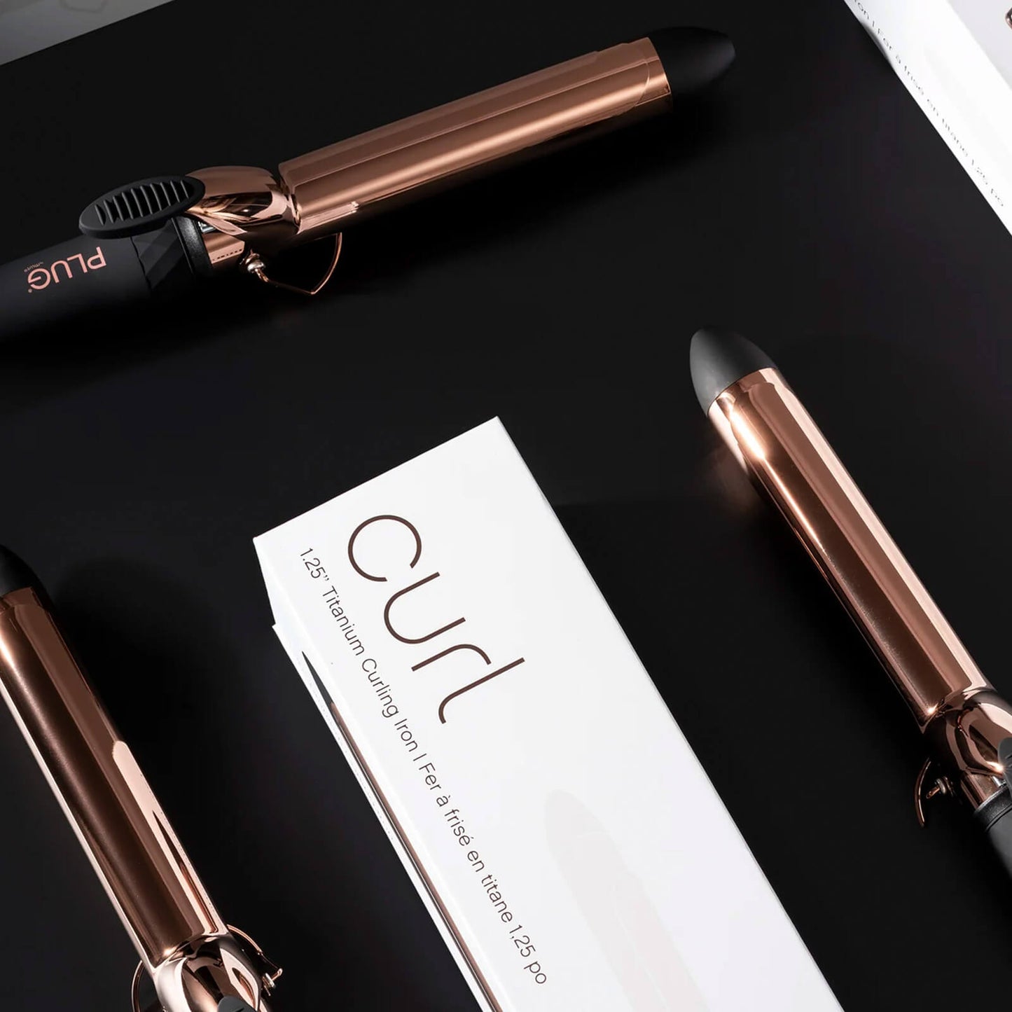 Plug By Must52 Curl Titanium Curling Iron — rose-gold titanium curling iron with its Curl carton on a black surface