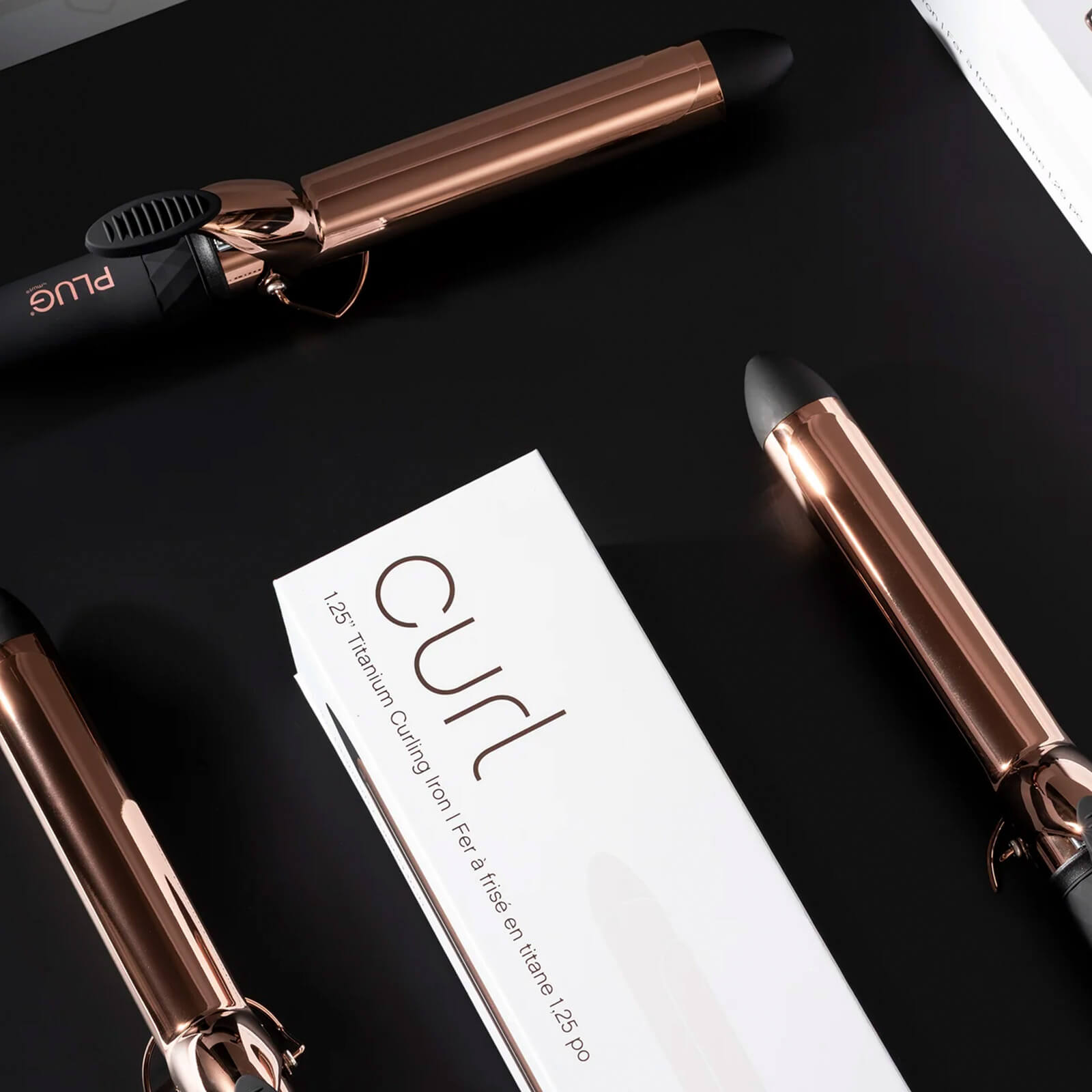 Plug By Must52 Curl Titanium Curling Iron — rose-gold titanium curling iron with its Curl carton on a black surface