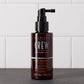American Crew Fortifying Scalp Treatment — 100 ml spray bottle standing on a dark counter against white tiles, label reading 3.3 Fl. Oz. / 100 mL