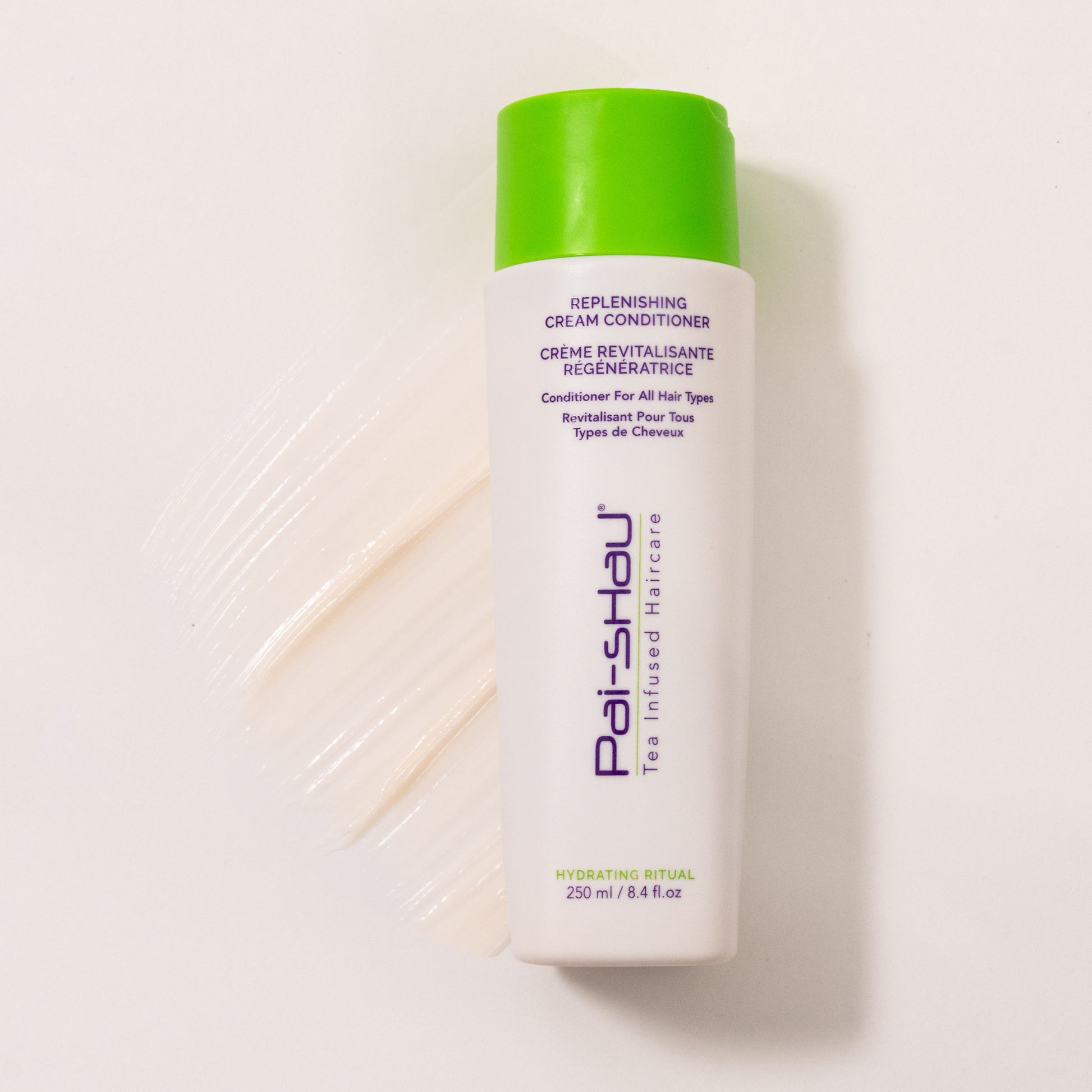 Pai-Shau - Replenishing Cream Conditioner — new-livery white 250 ml bottle lying flat beside a cream swatch