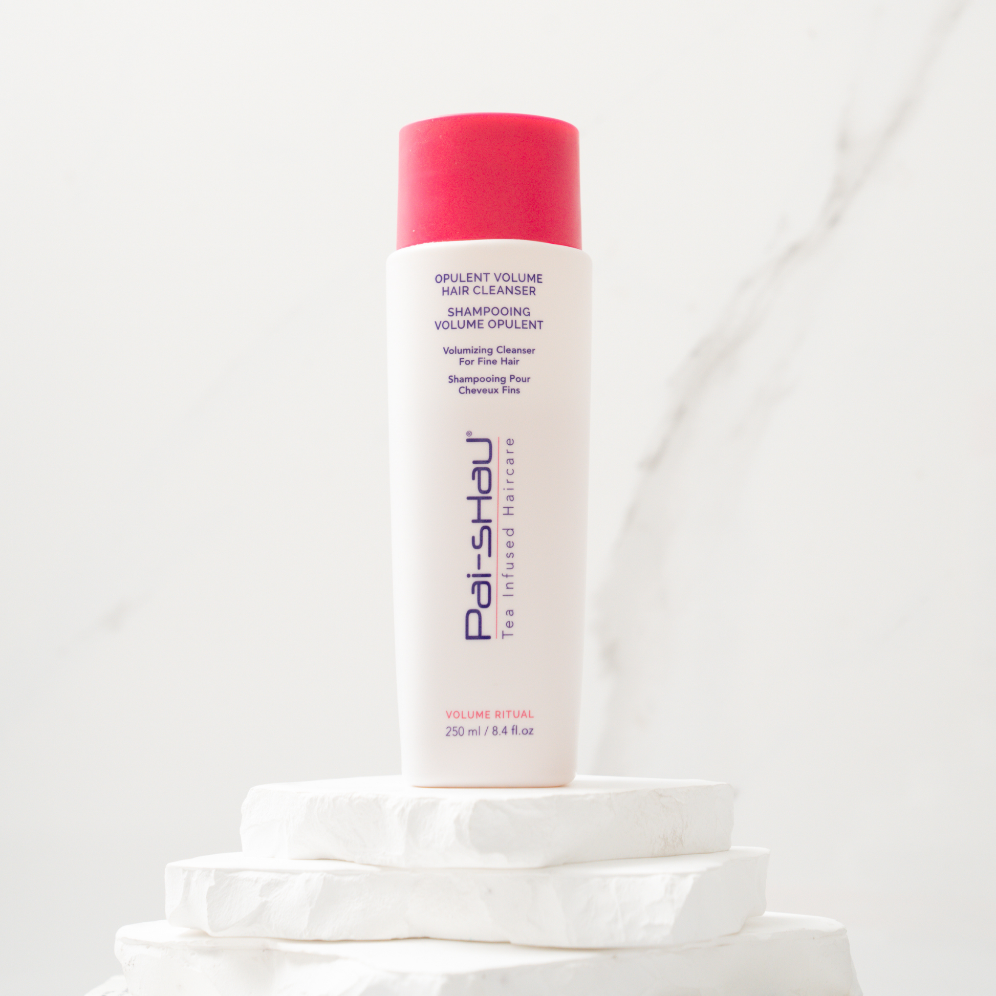 Pai-Shau Volumizing Shampoo — new-livery white 250 ml bottle on a stone plinth against marble