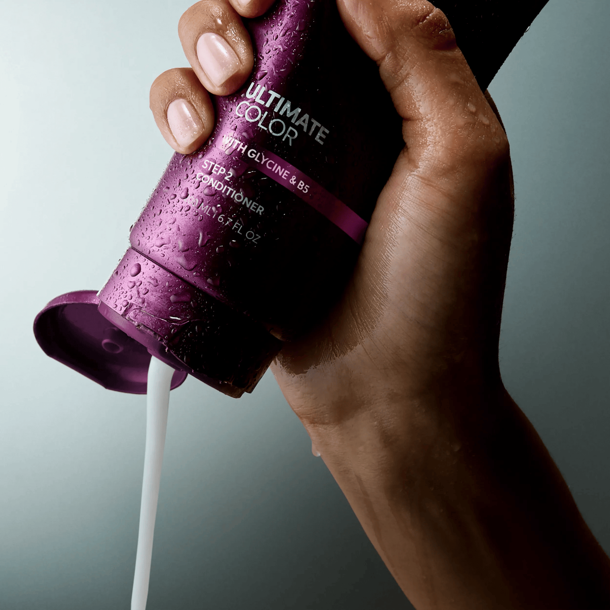 Wella Professionals Ultimate Color — Image of model's hand squeezing a bottle of the Ultimate Color conditoner. Text overlay reads " Smooth, creamy texture for porous strands".