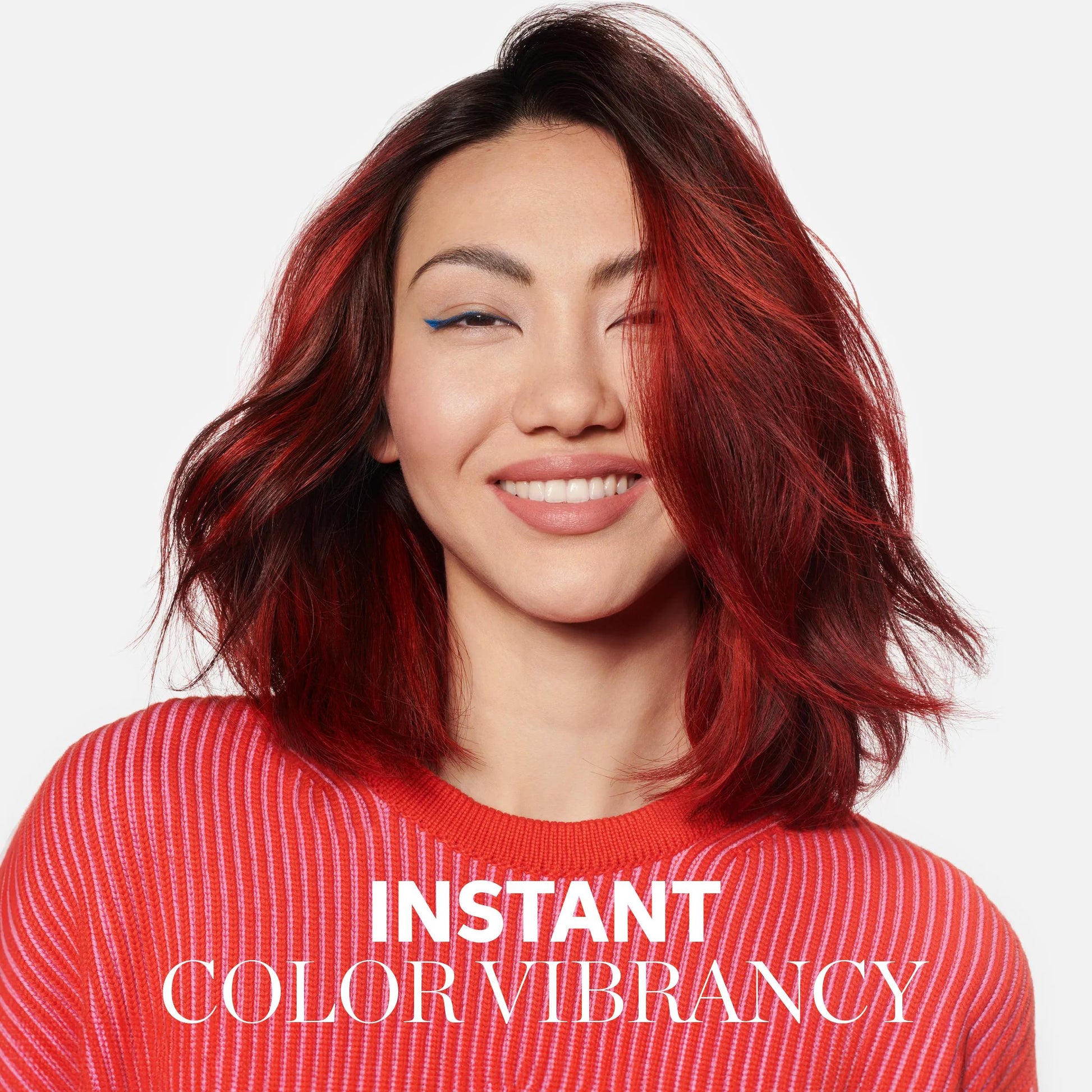 Wella Professionals Invigo Brilliance — Photograph of a young woman with voluminous shoulder-length red hair. She is smiling and wears a striped red jumper and blue winged eyeliner. Overlaid text reads 'instant color vibrancy'.