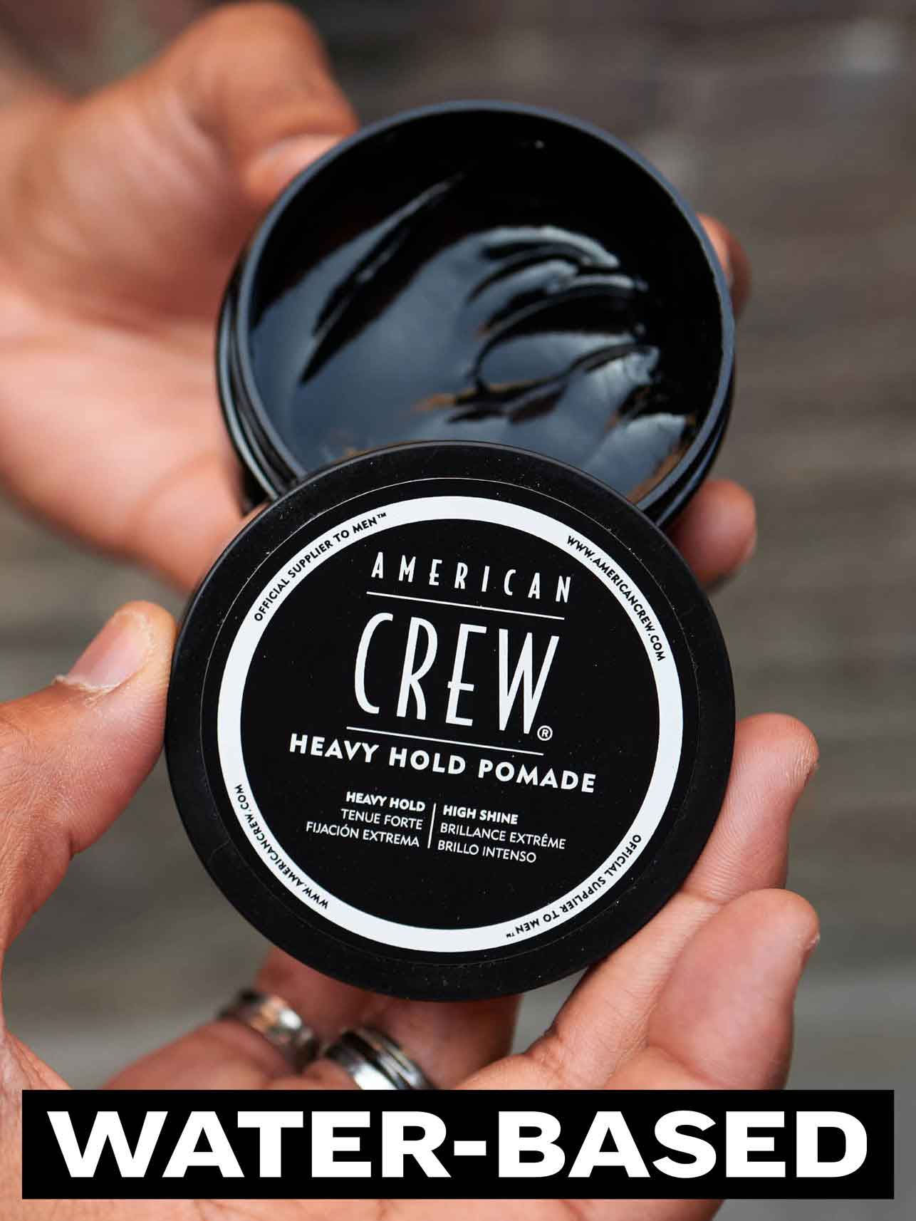 American Crew Heavy Hold Pomade — open 85 g tub held in hand showing the dark pomade texture, water-based formula